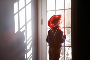 Girl wearing a cowboy hat looking out the window